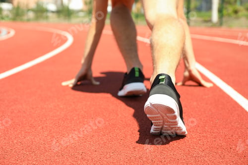 Preview: Sportsman low starting to run on red athletic track, close up