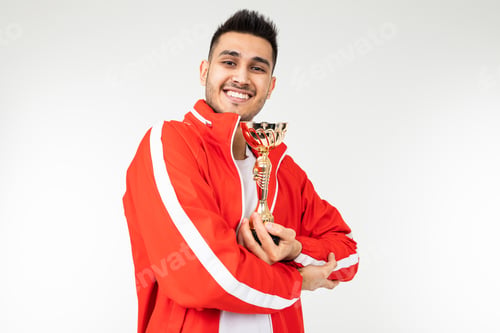 Preview: happy athlete in tracksuit with a golden winner cup on a white studio background