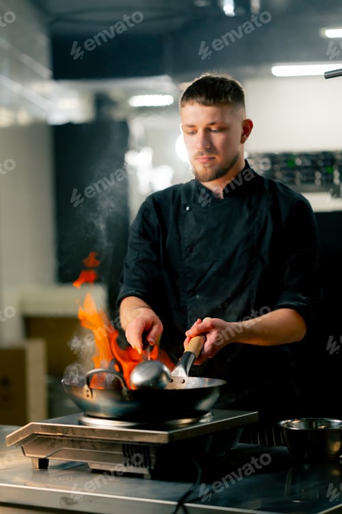 Preview: in professional kitchen the chef prepares wog noodles with vegetables on a large frying pan