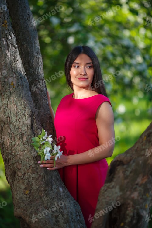 Vista previa: Retrato de una joven hermosa con un vestido rojo entre un floreciente jardín de primavera