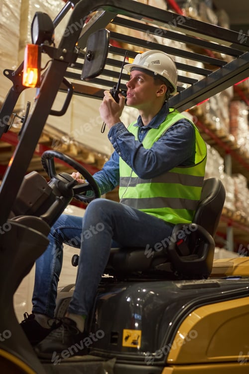 Preview: Worker driving forklift truck in warehouse speaking to portable radio