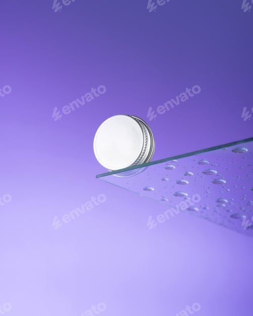 Preview: Manicure balm oil with cuticle shells in metal jar on glass with drops a very peri background
