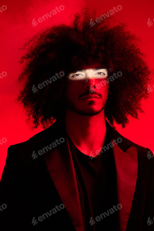 Preview: Fashion portrait of a man with curly hair on a red background, multinational, colored light, trendy