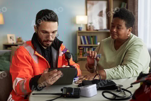 Preview: Young Male Paramedic Consulting Senior Black Woman Using Tablet