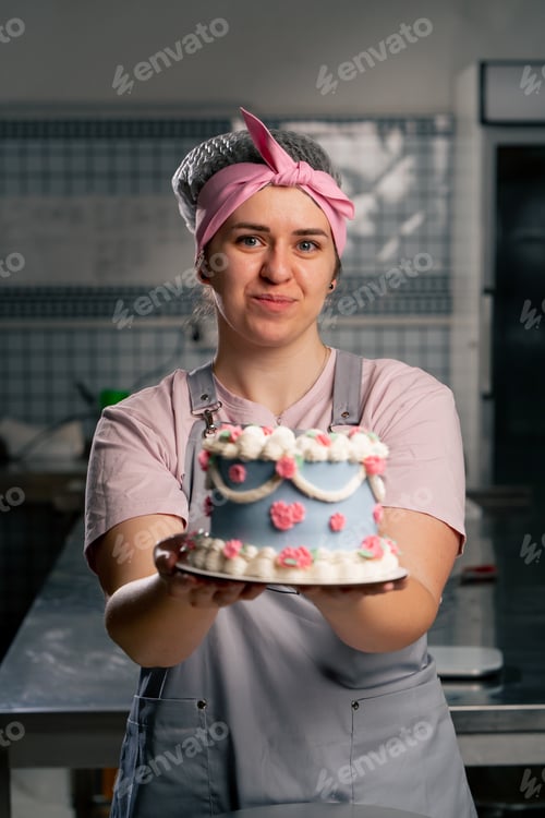 Preview: close-up in professional kitchen a female baker stands with a finished cake in her hands she smiling