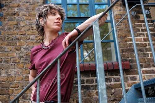 Preview: Androgynous female posing on metallic stairs out of building.