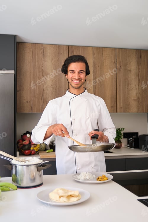 Preview: Indian chef holding frying pan preparing meal in a kitchen
