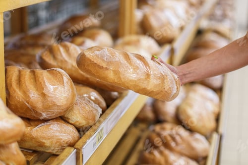 Preview: Young woman in the store buys fresh bread, loaf. Takes bread from the shelf. Close-up photo.