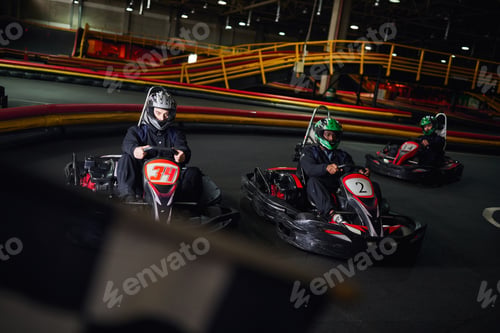 Preview: diverse men driving go kart near checkered black and white racing flag on blurred foreground