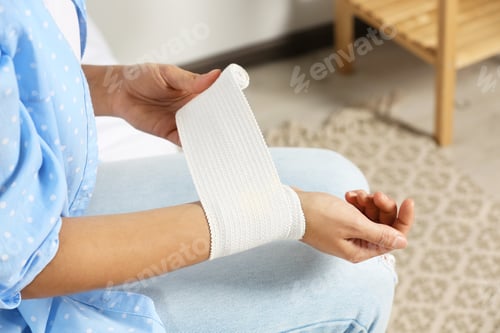 Preview: Young woman applying medical bandage onto wrist at home, closeup