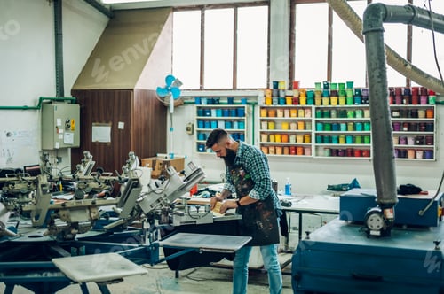 Preview: Male worker pressing ink on frame while using the printing machine in a workshop