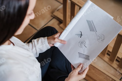 Preview: young woman assembling furniture at home reading instructions. DIY concept