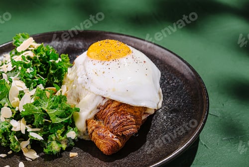 Preview: Delicious croissant topped with fried egg and greens on plate
