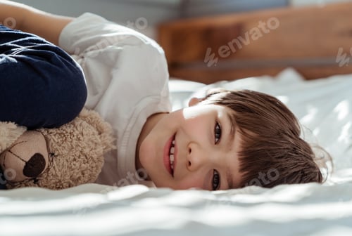 Preview: Portrait of little happy toddler boy lying on bed with his teddy bear plush toy