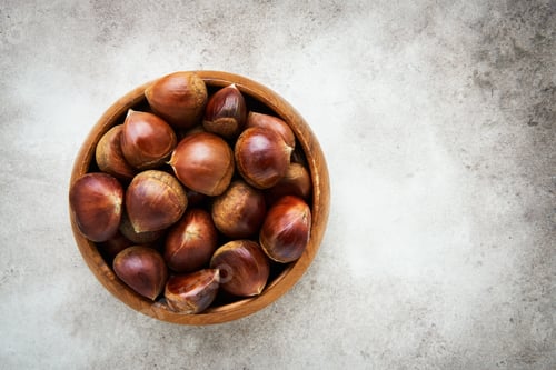 Preview: Pile of fresh sweet chestnuts in a bamboo bowl over grey background. Top view, copy space