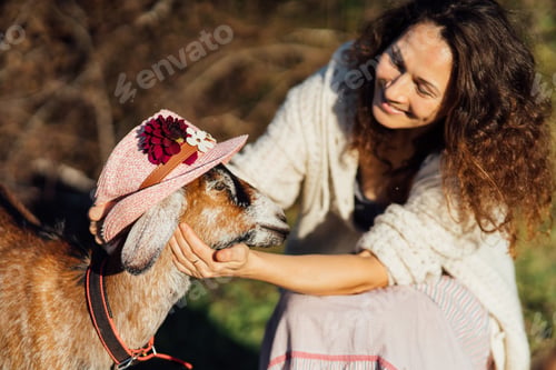 Preview: Woman in a hat and curly hair bonding with goats on a farm
