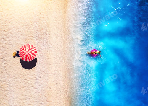 Preview: Aerial view of a woman in the sea, sandy beach and red umbrella