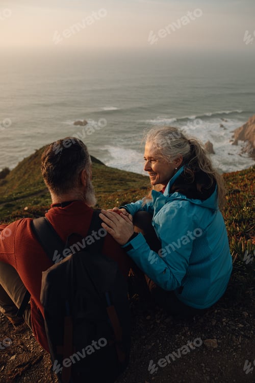 Preview: Senior couple enjoying views on ocean sitting on top of cliff together