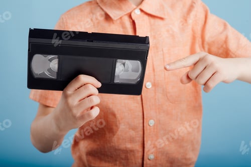 Preview: close up, little boy pointing to video tape, isolated on blue background,