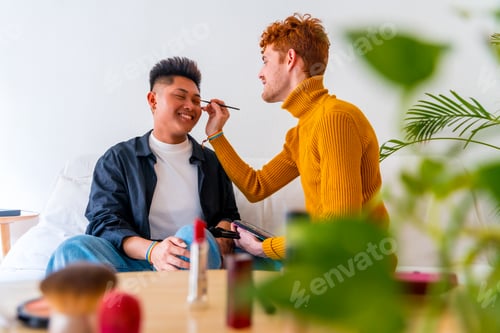 Preview: Beautiful gay couple putting on makeup and having fun being romantic indoors at home, lgbt concept