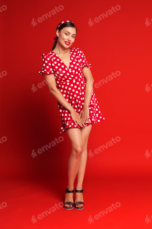 Preview: Woman in red polka dot dress striking a playful pose against a bright red background