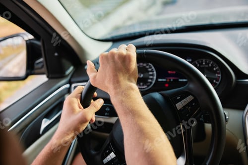 Preview: Hands gripping the steering wheel of a car while driving on a road