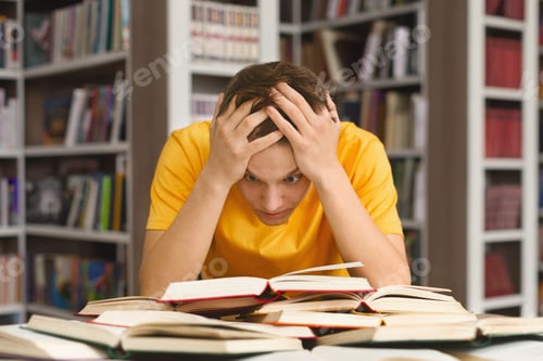 Preview: Exhausted guy holding his head and reading book in library