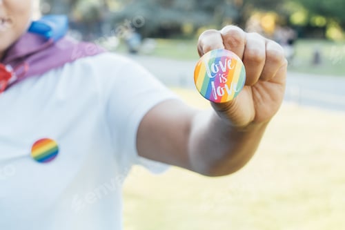 Preview: Closeup of LGBTQ rainbow flag pin in the hand of young lesbian activist. Love is love message.