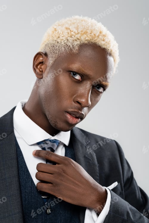 Preview: portrait of blonde african american man in suit adjusting tie isolated on grey