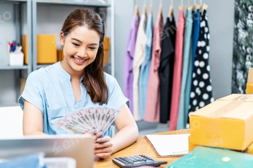 Preview: Young asian woman holding US dollars money lot of money happy and proud smile work at home