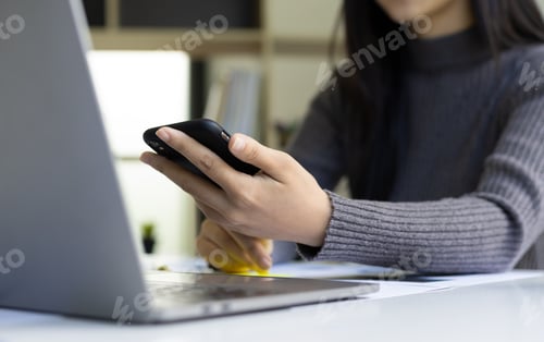 Preview: Close up modern business woman in office working on laptop and using smartphone.