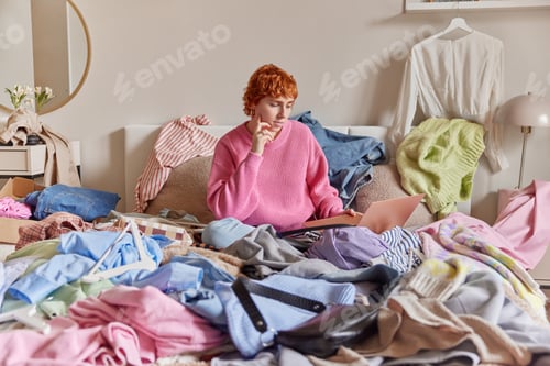 Preview: Photo of redhead young woman in pink knitted jumper concentrated in laptop poses on bed with pile of