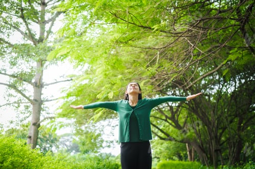 Preview: An Asian woman is standing happily in a green forest park, enjoying the fresh air and nature