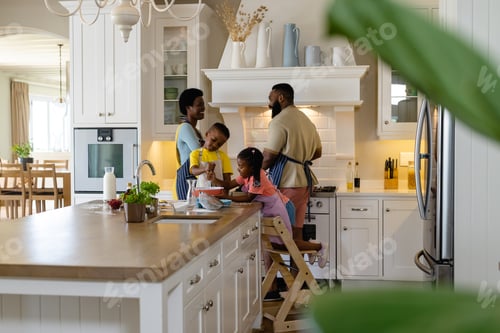 Preview: African american siblings mixing batter in bowl on kitchen island with parents in background at home
