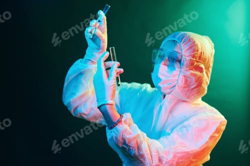 Preview: Nurse in mask and white uniform standing in neon lighted room and holding tubes with samples