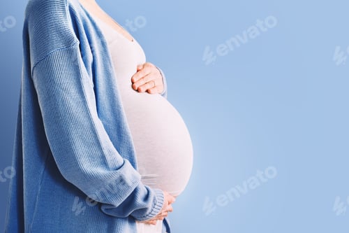 Preview: Beautiful pregnant woman hugging her belly in blue background.
