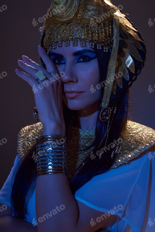 Preview: Portrait of beautiful woman in Egyptian headdress posing in blue light on brown background