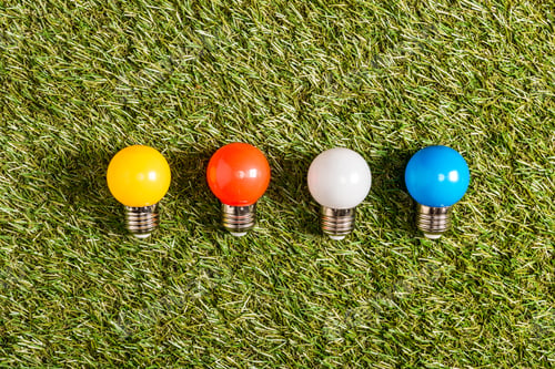 Preview: flat lay of colorful fluorescent lamps on green grass, energy efficiency concept