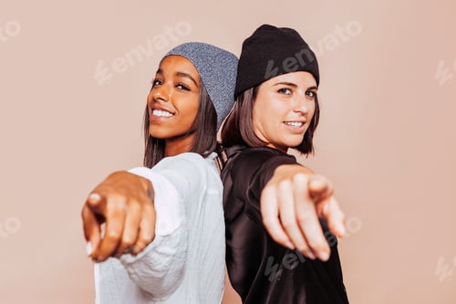 Preview: Two stylish smiling woman point finger at you at studio