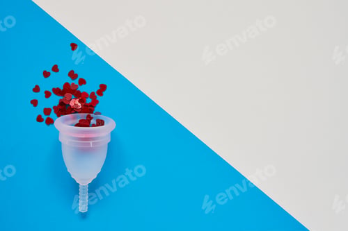 Preview: White menstrual cup with red glitters on blue background. Women health concept. Copy space