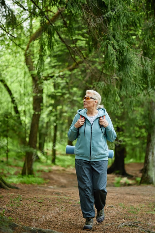 Preview: Senior Caucasian Woman Hiking in Forest Carrying Yoga Mat and Backpack
