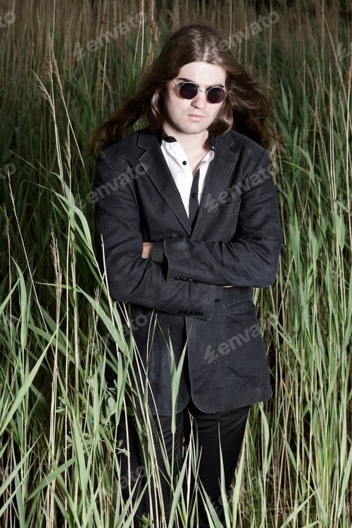 Preview: Young Man With Long Brown Hair Wearing Sunglasses And Black Suit Standing In Field With Long Grass