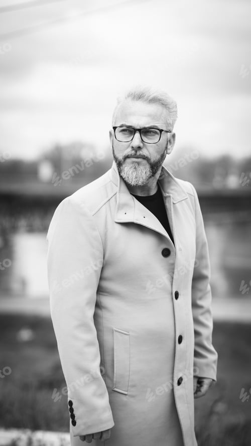 Preview: Grayscale of a confident man with gray hair wearing a stylish brown coat on background of a bridge