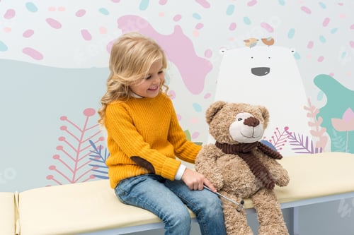 Preview: adorable little girl doing neurology examination of teddy bear while sitting on sofa