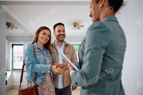 Preview: Happy couple of real estate buyers handshaking with their agent in a new house.