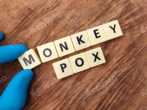 Preview: Hand holding toys word with the word MONKEY POX on wooden background.