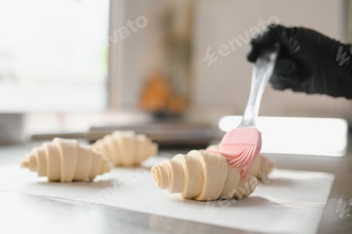 Preview: Baker spreading egg wash on croissants in bakery