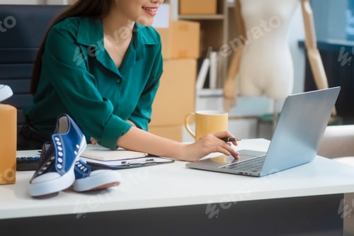 Preview: Young Asian woman manages SME shoe store, using devices to check orders, addresses, and packaging.