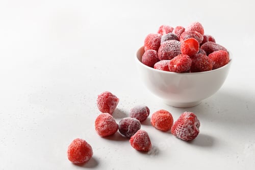 Preview: Frozen strawberries and cherry in bowl on white background. Copy space.