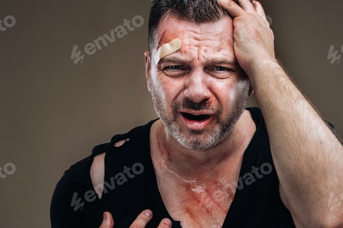 Preview: Against a gray background stands a battered angry man in a black T-shirt with wounds